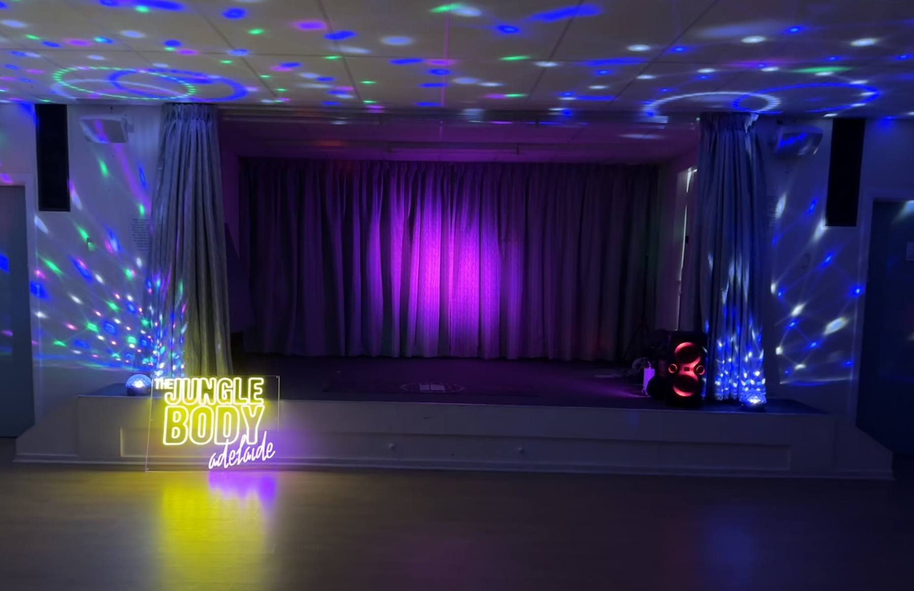 The Ascot Park hall stage lit purple with disco lights and the Jungle Body Adelaide neon sign